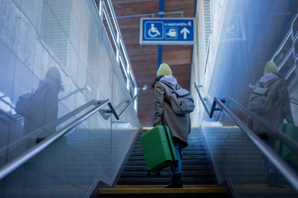 Young woman traveler tourist going up the stairs with luggage in a train station. Rear view.