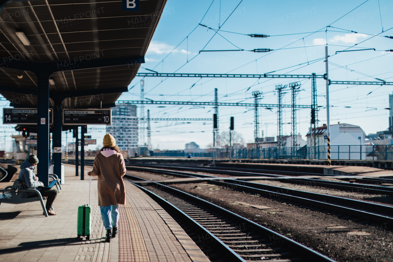 A happy young traveler woman with luggage waiting for train at train station platform