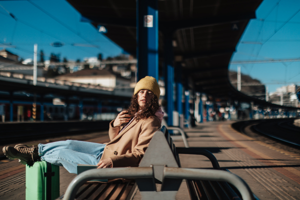 A young traveler woman sitting alone at train station platform with luggage.