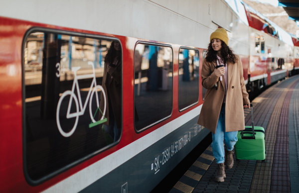 A happy young traveler woman with luggage and cup of coffee boarding in the train at train station platform