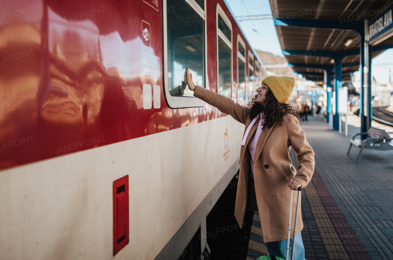 A young traveler woman with luggage standing in platform and saying goodbye, waveing somebody in train