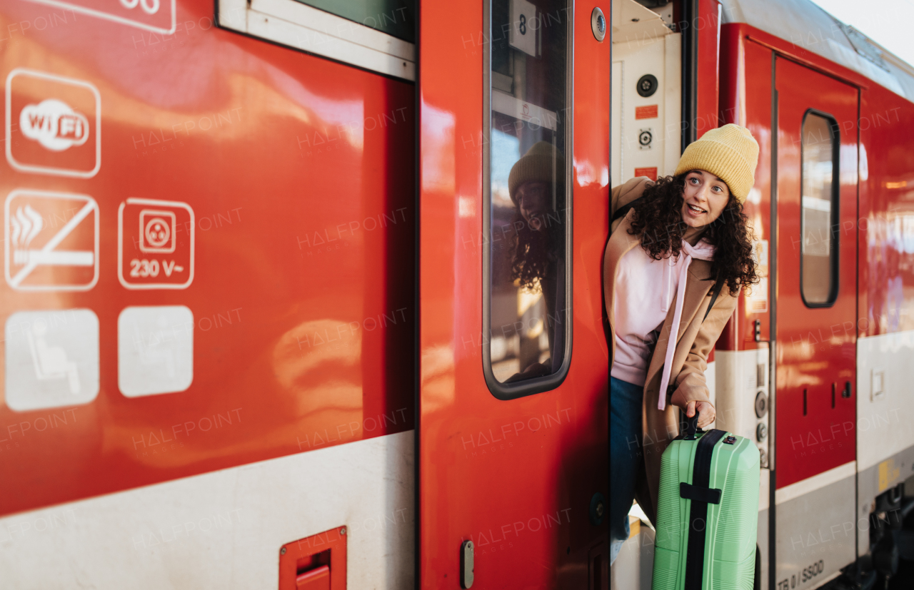 A happy young traveler woman with luggage getting off the train at train station platform