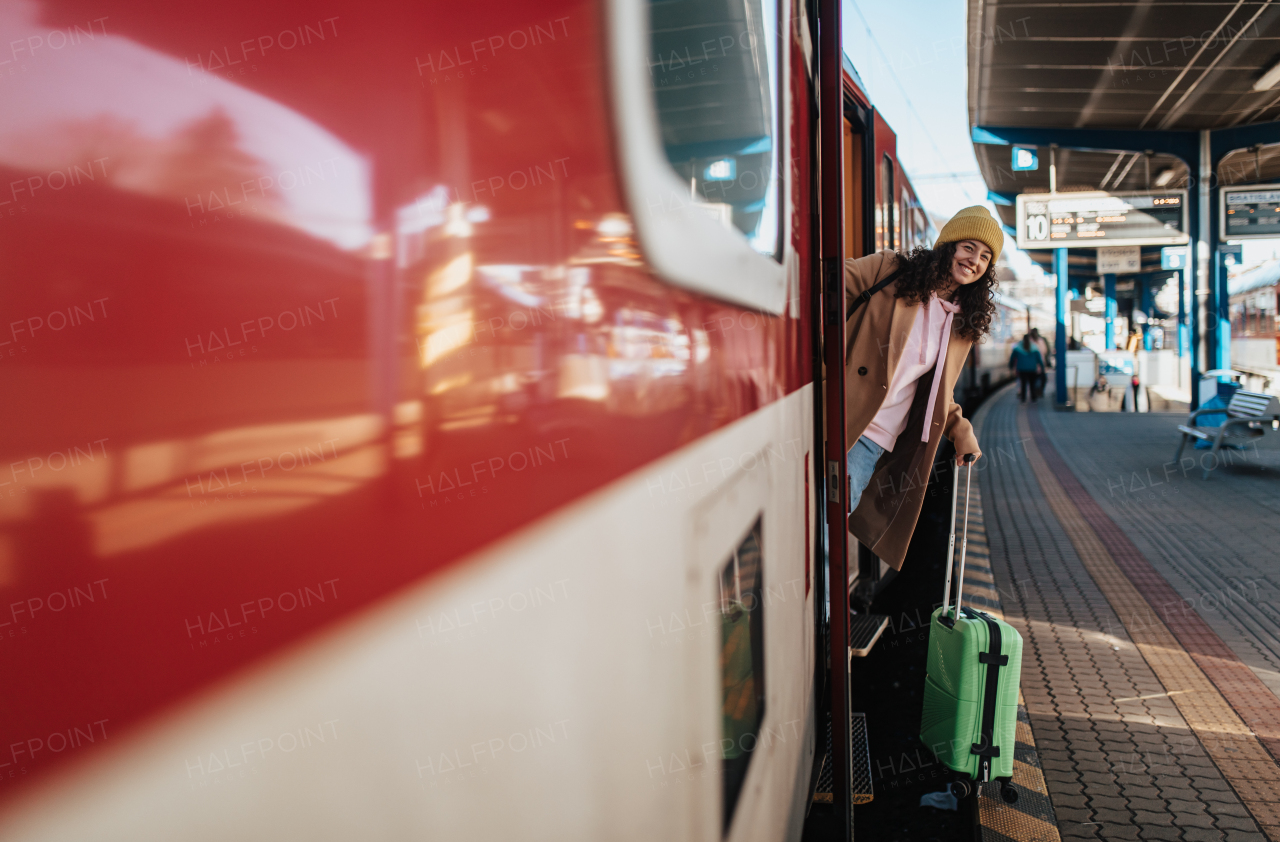 A happy young traveler woman with luggage getting off the train at train station platform