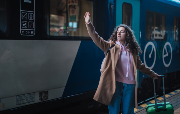 A young traveler woman with luggage standing in platform and saying goodbye, waveing somebody in train