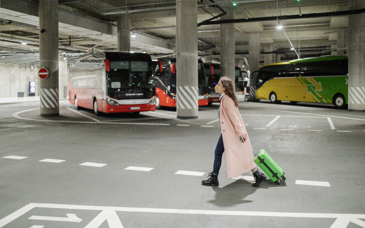 Alone woman traveler with ffp2 respirator going trough bus station with luggage. Traveling during covid pandemic.