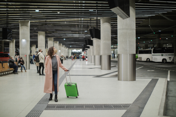 Alone woman traveler with ffp2 respirator going trough bus station with luggage. Traveling during covid pandemic.