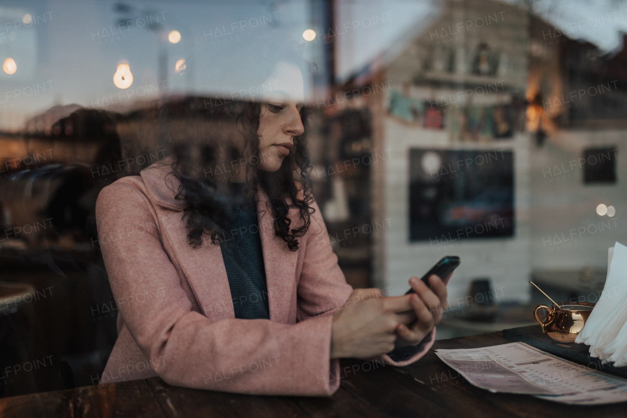 A young woman drinking tea and texting while enjoying her leisure time alone in cafe