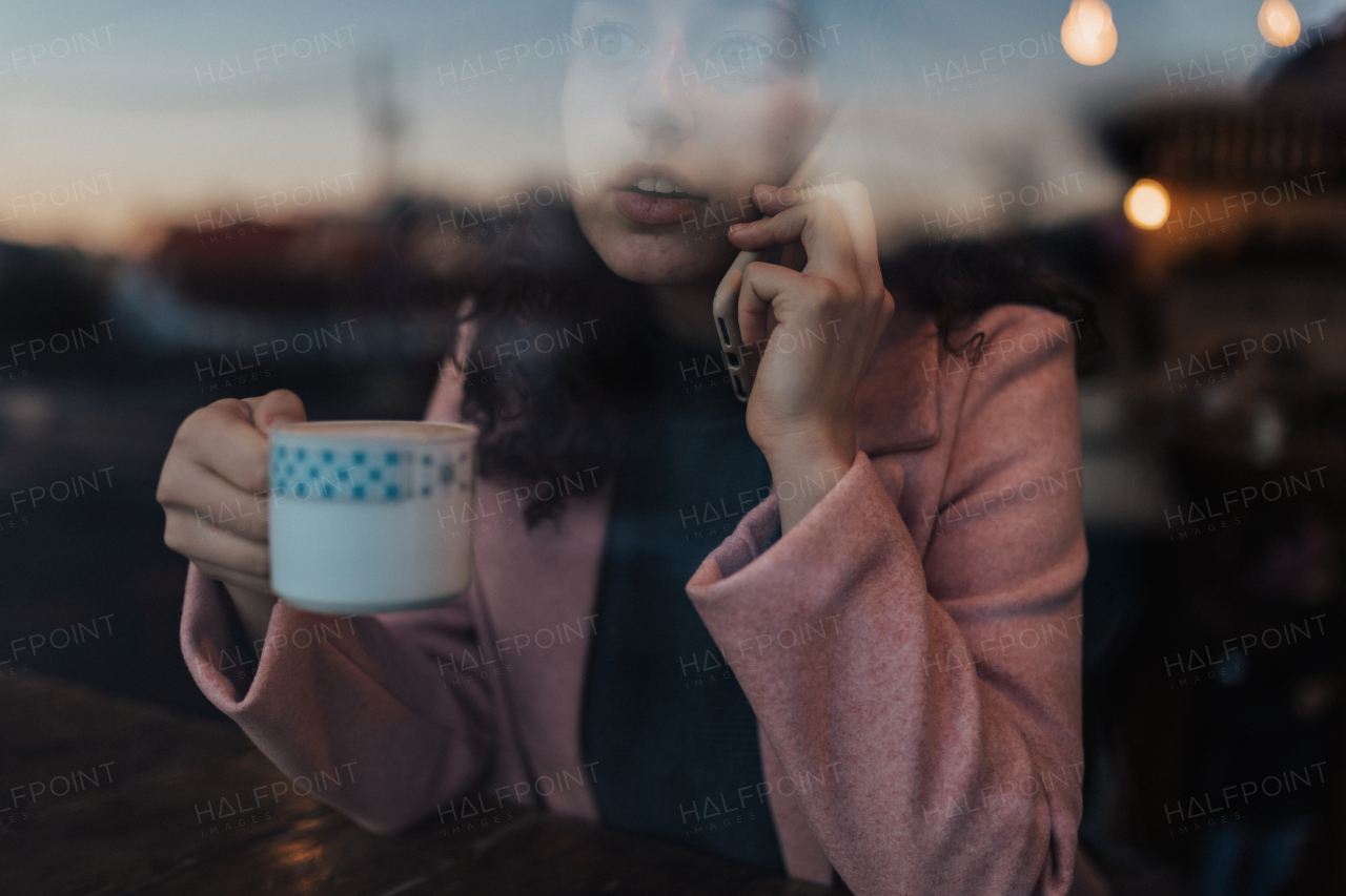 A young woman drinking tea and looking out of the cafe window while enjoying her leisure time alone