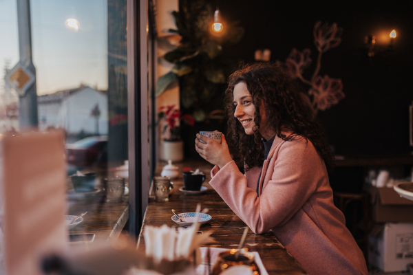 A young woman drinking tea and looking out of the cafe window while enjoying her leisure time alone