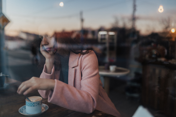 Sad,pensive young woman drinking a coffee and looking out of the cafe window.