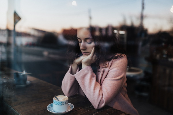 Sad,pensive young woman drinking a coffee and looking out of the cafe window.