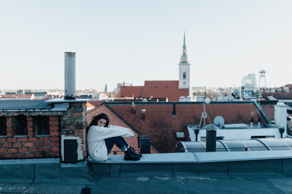 An unhappy young woman resting and sitting on the roof with city view.