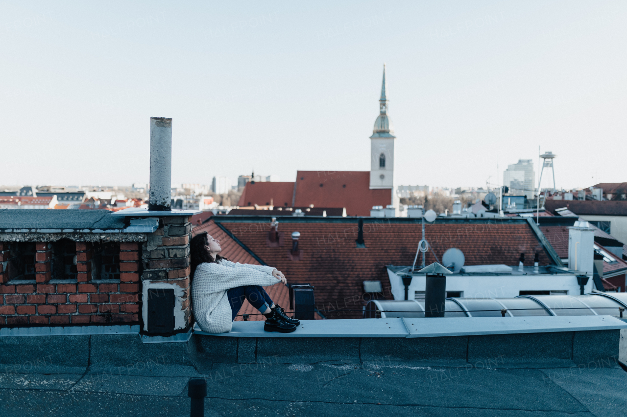 An unhappy young woman resting and sitting on the roof with city view.