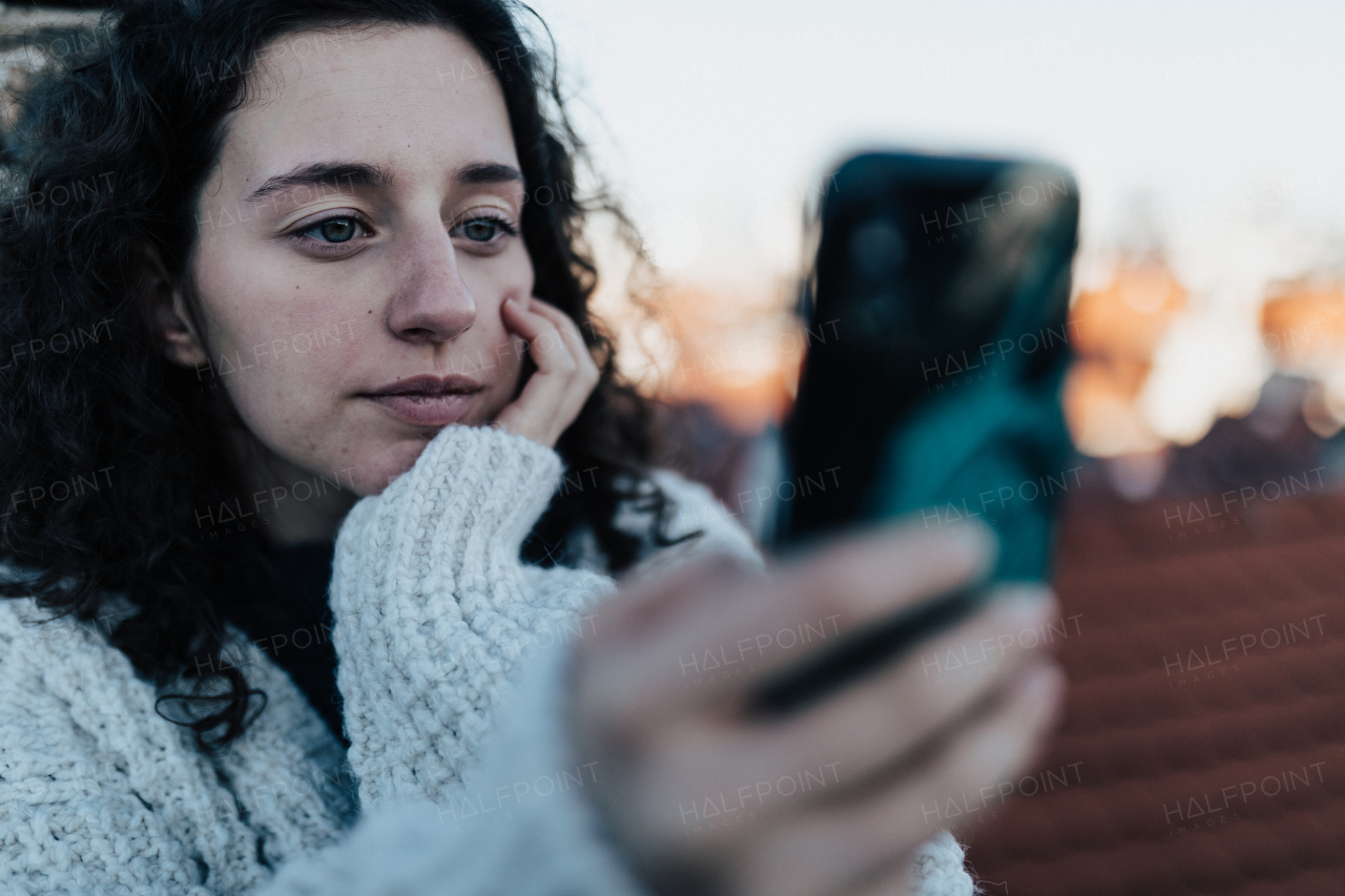 An unhappy young woman resting and sitting on the roof with city view and taking selfie.