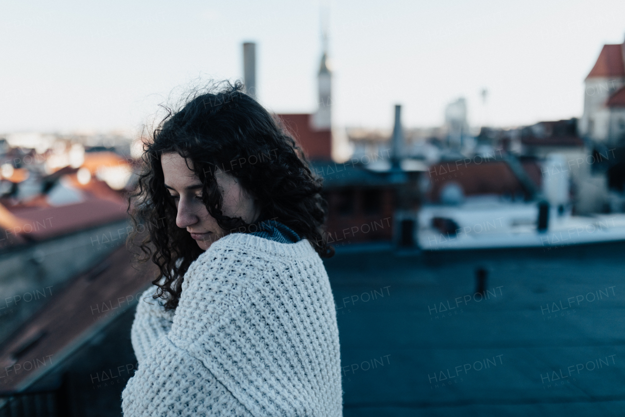 An unhappy, pensive young woman standing on the roof with city view.