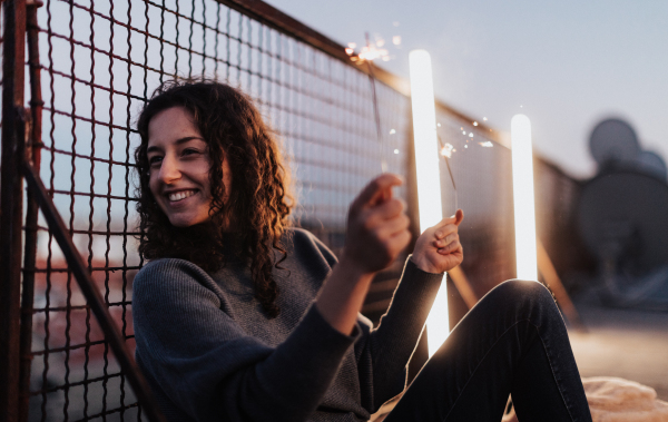 A young woman with sparklers having fun at rooftop in the city, close up.