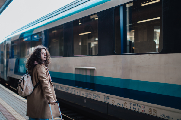 A happy young traveler woman with luggage waiting for train at train station platform