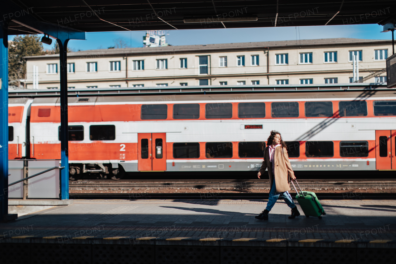 A young traveler woman with luggage waiting for train at train station platform. Train in the background.