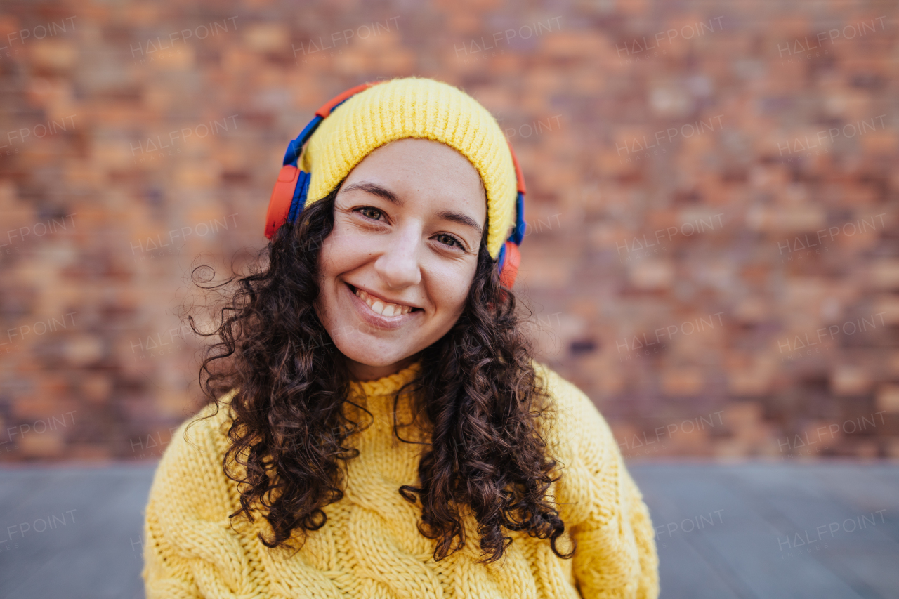 A portrait of happy young woman with headphones in city street, looking at camera.