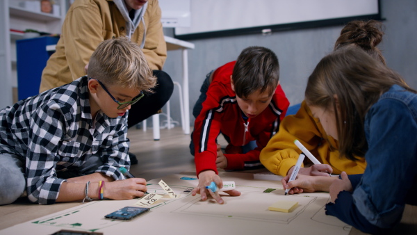 A group of happy kids with their teacher working on project together at classroom.