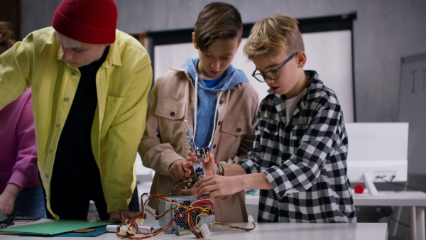 A group of happy kids with their science teacher with electric toys and robots at robotics classroom