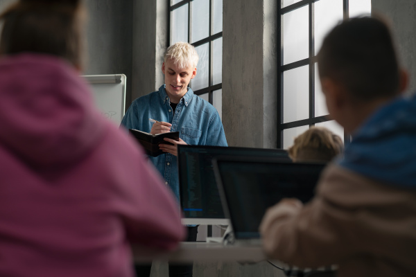 A school teacher standing in front of pupils and writing notes in computer classroom at school