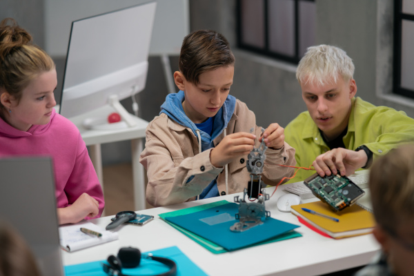 A group of happy kids with their science teacher with electric toys and robots at robotics classroom