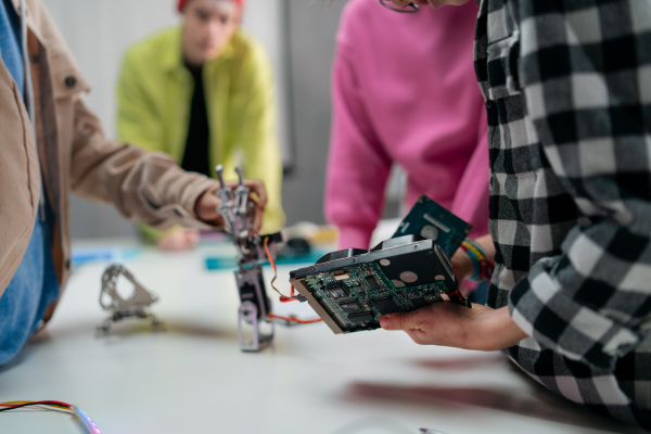 Kids with a teacher working together on project with electric toys and robots at robotics classroom, close-up