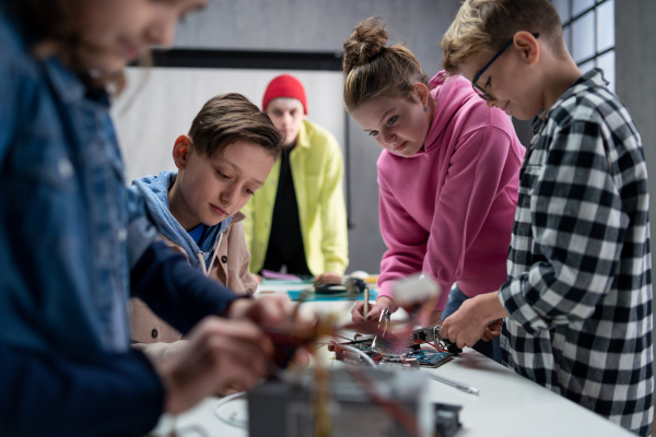 A group of happy kids with their science teacher with electric toys and robots at robotics classroom