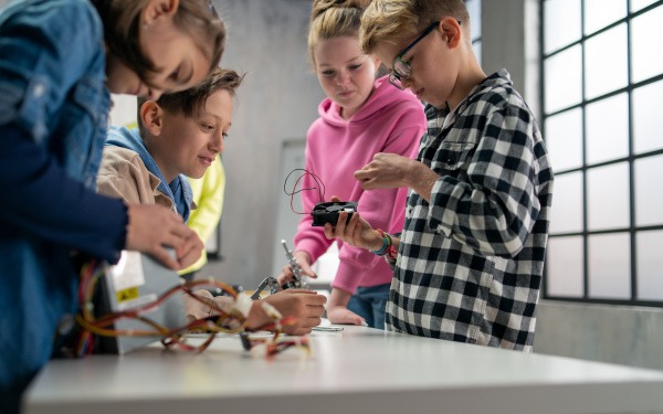 A group of happy kids with their science teacher and electric toys, robots at robotics classroom