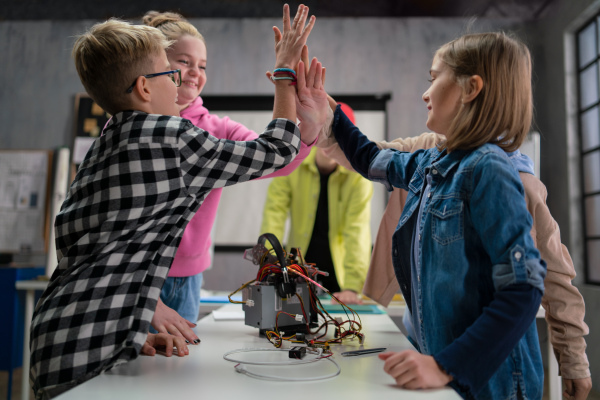 A group of happy kids with their science teacher with electric toys and robots at robotics classroom