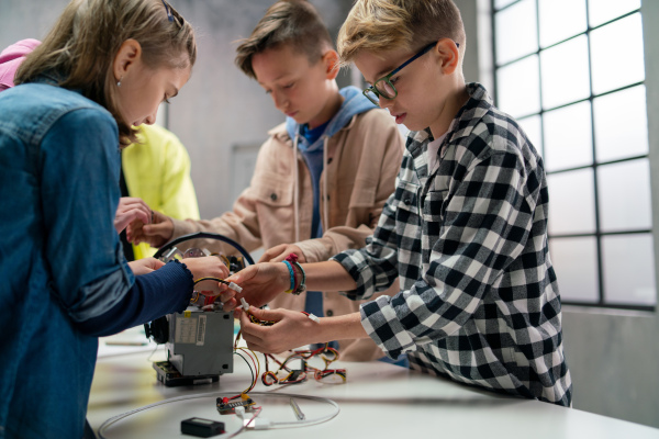 A group of happy kids with their science teacher with electric toys and robots at robotics classroom