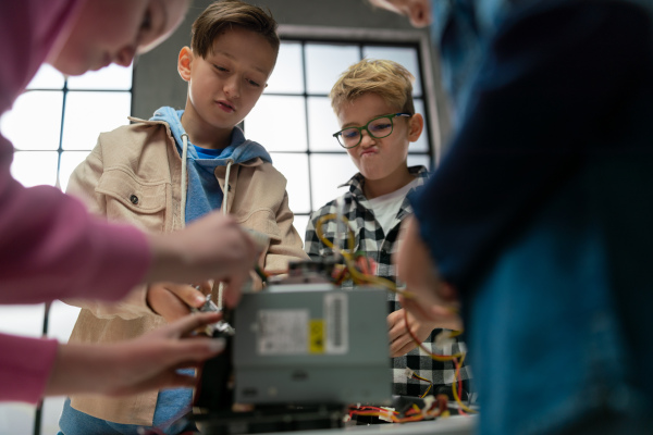 Kids with a teacher working together on project with electric toys and robots at robotics classroom.