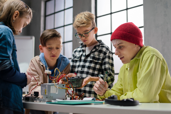 A group of happy kids with their science teacher with electric toys and robots at robotics classroom