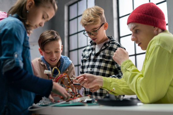 A group of happy kids with their science teacher with electric toys and robots at robotics classroom