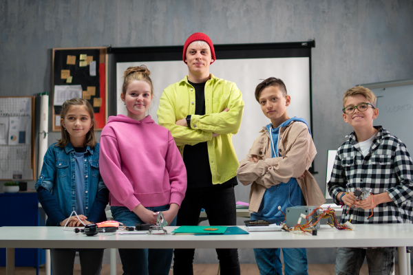 A group of happy kids with their science teacher with electric toys and robots at robotics classroom