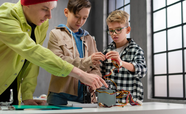 A group of happy kids with their science teacher with electric toys and robots at robotics classroom