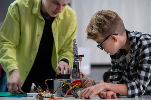 Student with teacher working together on project with electric toys and robots at robotics classroom