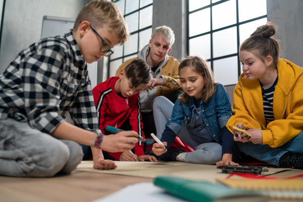 A group of happy kids with their teacher working on project together at classroom.