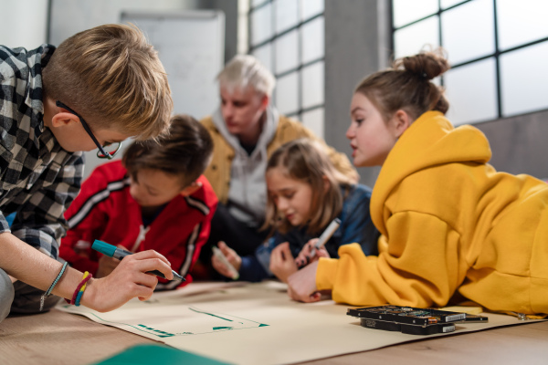 A group of happy kids with their science teacher with electric toys and robots at robotics classroom