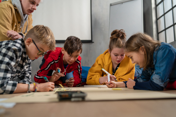 A group of happy kids with their science teacher with electric toys and robots at robotics classroom