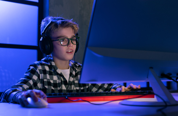 A young gamer boy with headphones playing computer video game.