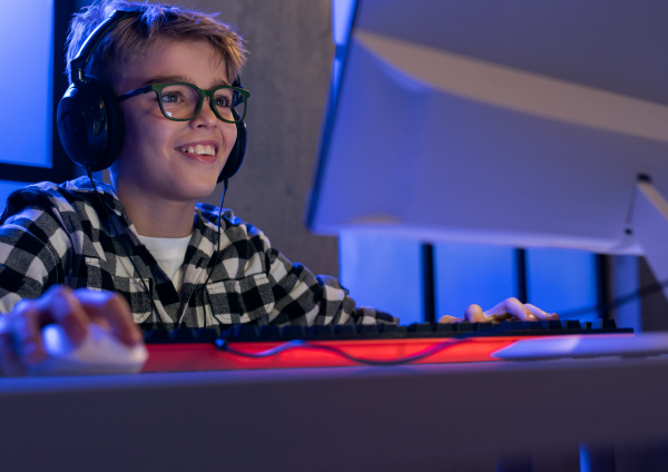 A young gamer boy with headphones playing computer video game.