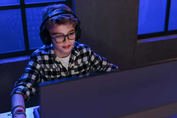 A young gamer boy with headphones playing computer video game.