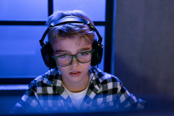 Young gamer boy with headphones playing a computer video game.