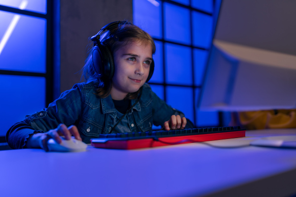 Young gamer girl with headphones playing a computer video game.