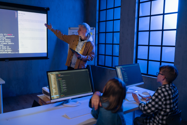 A teacher giving computer science lecture to young students in dark room. Room. Explaining Information Technology.