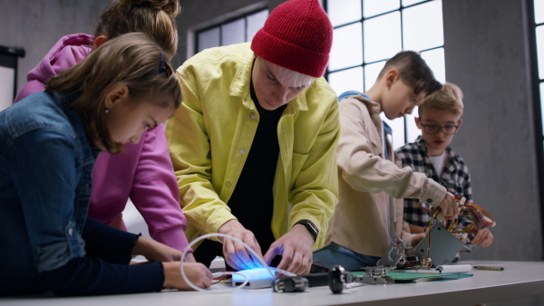 A group of happy kids with their science teacher with electric toys and robots at robotics classroom