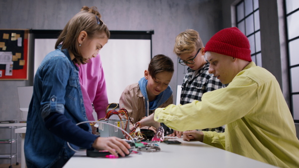 A group of happy kids with their science teacher with electric toys and robots at robotics classroom