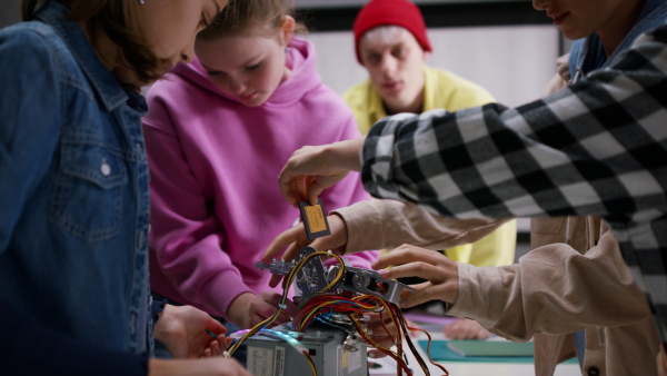 A group of happy kids with their science teacher with electric toys and robots at robotics classroom